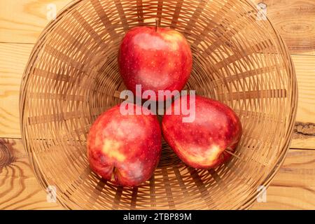 Three red organic apples in a straw plate on a wooden table, macro, top view. Stock Photo