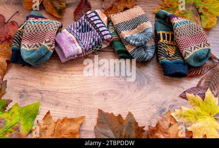 Folded pairs of colourful Winter woollen socks within a circle of fallen leaves on a wooden background. Stock Photo