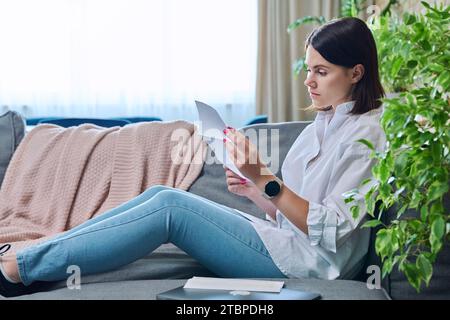 Serious young woman reading official paper letter, sitting at home Stock Photo