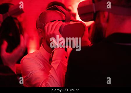 In a red-lit realm of virtual wonder, two men explore a shared digital frontier, surrounded by an enthusiastic crowd, embracing the future of immersiv Stock Photo