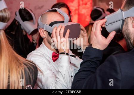 In a red-lit realm of virtual wonder, two men explore a shared digital frontier, surrounded by an enthusiastic crowd, embracing the future of immersiv Stock Photo