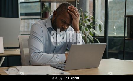 Overworked African American mature man working laptop in office suffer with eye strain exhausted sick fatigued male senior businessman feel pain Stock Photo