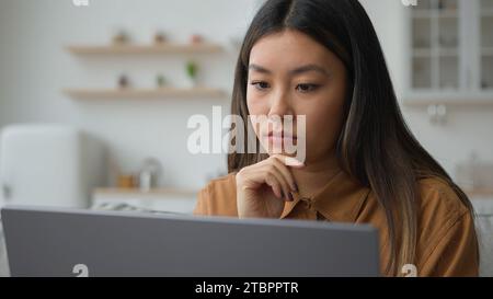 Smart pensive Asian chinese woman 30s businesswoman work from home kitchen thoughtful writer think business plan contemplate search media online on Stock Photo