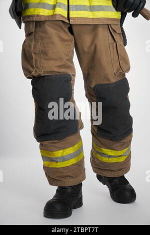 Unrecognizable firefighter walking after hard working day. Crop view of fireman in uniform and black boots, isolated on white studio background. Concept of firefighter, work, uniform. Stock Photo