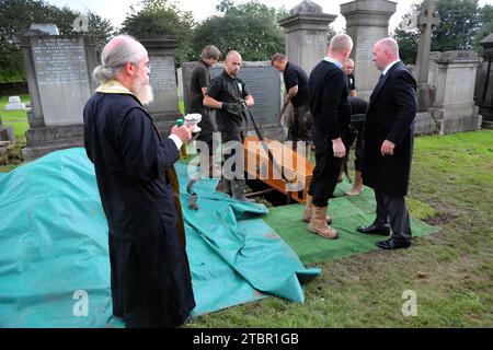 Glasgow Scotland Greek Orthodox Funeral at Glasgow Necropolis - Priest Holding Bottle of Olive Oil as the Coffin is Manually Lowered into the Grave Stock Photo