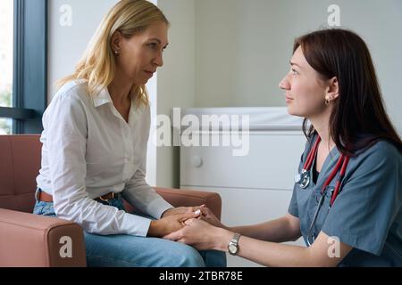 Caring physician comforting sad woman in clinic lobby Stock Photo