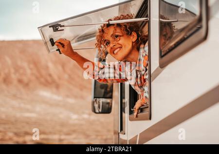 Happy tourist enjoy parking destination opening the window of a modern camper van and looking outside with a smile. One adult alone traveler woman admire outdoors. Travel people lifestyle. Alternative Stock Photo