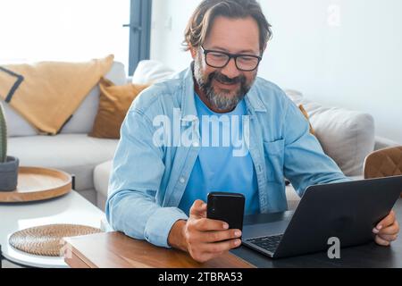 One man at home using mobile phone and laptop on the table. Concept of online small business and smart working people lifestyle. Communication with cell and computer. Technology. Modern adult people Stock Photo