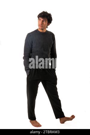 A man in a black sweater and black pants, walking around, with hands in pockets, full figure shot isolated on white Stock Photo