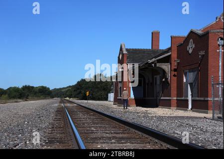 Abandoned train station is at Strong City, Kansas.  Formerly a stop by the Atchison, Topeka & Santa Fe Railroad.  Visitor admires the American Craftsm Stock Photo