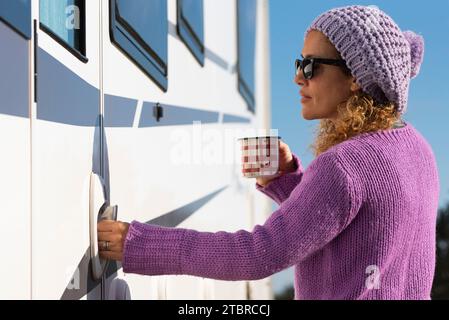 One pretty woman open the door of her camper van ready to leave and start travel adventure alone, Empowerment female people driving rv vehicle. Alone tourist lady with violet pullover enter on camper Stock Photo