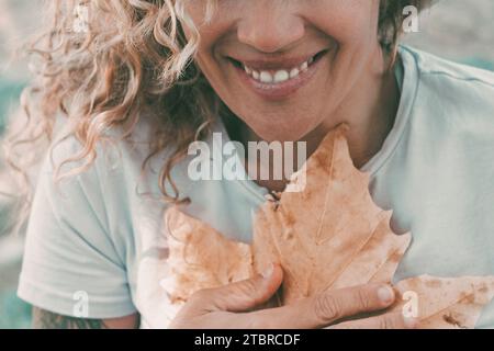 People love nature and feeling contact environment. One cheerful woman smile and hug to protect a big autumn yellow maple leaf on her chest. Concept of environment lifestyle. One adult female outdoor Stock Photo