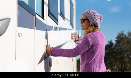 One pretty woman open the door of her camper van ready to leave and start travel adventure alone, Empowerment female people driving rv vehicle. Alone tourist lady with violet pullover enter on camper Stock Photo