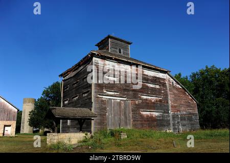 Unique barn structure has cupola on top.  Barn at one time was painted white, and you can see the weathered remains at the top.  Stone water well sits Stock Photo