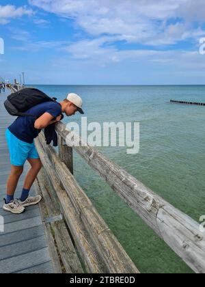 Germany, Mecklenburg-Western Pomerania, peninsula Fischland-Darß-Zingst, a teenage boy looks over the railing of the pier Zingst into the sea water Stock Photo