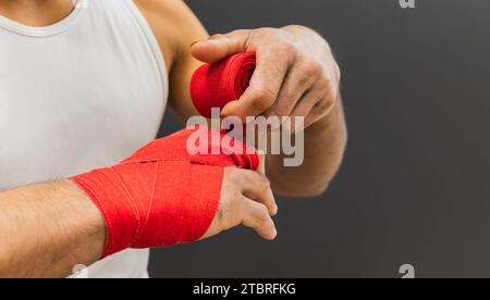 Horizontal photo hands of young adult mixed race man, putting red bandages on his hands to box, on gray copy space background. Sports and recreation c Stock Photo