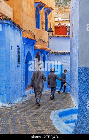 Muslim man wearing traditional Islamic djellaba / jillaba walking through narrow blue alleyway in medina of the city Chefchaouen / Chaouen, Morocco Stock Photo