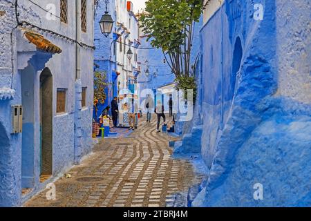 Moroccans in narrow alleyway with blue houses in medina / historic old town of the city Chefchaouen / Chaouen, Morocco Stock Photo