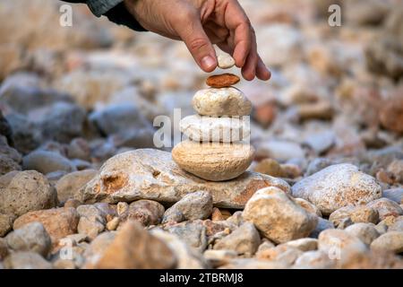 Zen-style stone pyramid in a natural setting with a hand that gently places a stone on top, which conveys peace, harmony and respect for nature Stock Photo