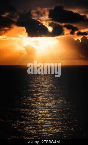 A beautiful orange and pink sunset sky over the ocean horizon, with wispy clouds illuminated by the setting sun Stock Photo