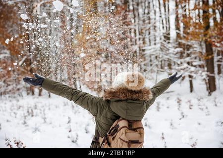 Cheerful woman playing with snow at winter forest. Happiness and mindfulness during enjoying walk outdoors Stock Photo