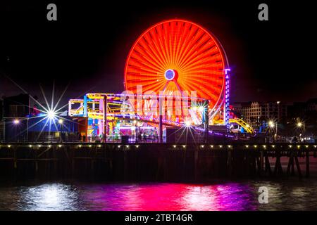 Pacific Park at Santa Monica Pier, Santa Monica, California, with the Ferris wheel and roller coaster illuminated at night reflected in the ocean Stock Photo