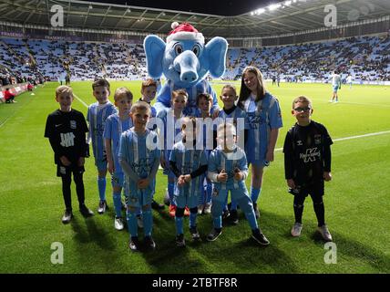 Young Coventry City fans pose with club mascot Sky Blue Sam before the Sky Bet Championship match at the Coventry Building Society Arena, Coventry. Picture date: Friday December 8, 2023. Stock Photo