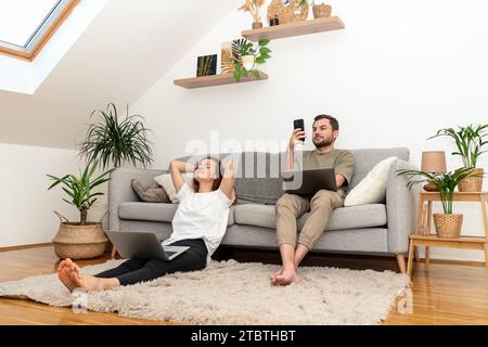 Young couple at home using their laptops and smart phones.. Portable information devices and people domestic lifestyle. Stock Photo