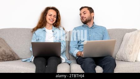 Couple in denim shirts sitting on sofa and using their laptops. Safety and security of personal data on the Internet. Stock Photo