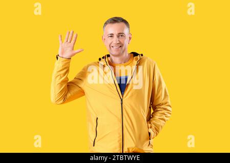 Mature man in jacket waving hand on yellow background Stock Photo