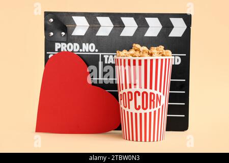 Movie clapper with bucket of popcorn and paper heart on yellow background. Valentine's Day celebration Stock Photo