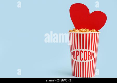 Bucket of popcorn with paper heart on blue background. Valentine's Day celebration Stock Photo