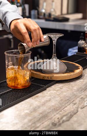 Bartender pouring whiskey out of a jigger and making smoked whiskey cocktail drink Stock Photo