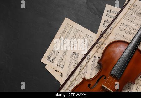 Violin, bow and music sheets on black table, top view. Space for text Stock Photo