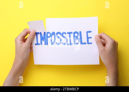 Motivation concept. Woman making word Possible from Impossible by tearing paper on yellow background, top view Stock Photo