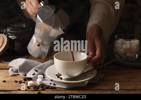 Woman pouring aromatic coffee from moka pot into cup at wooden table, closeup Stock Photo