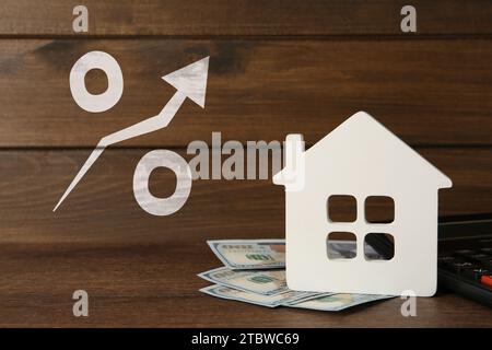 Mortgage rate rising illustrated by percent sign with upward arrow. House model, money and calculator on wooden table Stock Photo