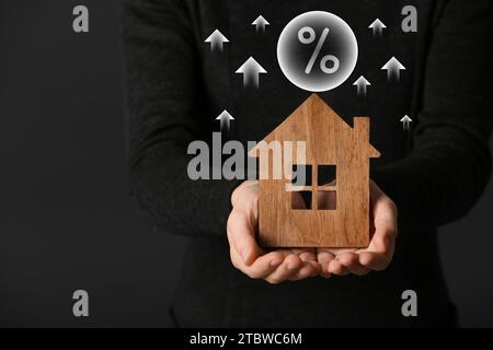 Mortgage rate rising illustrated by upward arrows and percent sign. Woman with wooden house on dark background, closeup Stock Photo