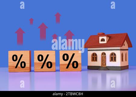 Mortgage rate rising illustrated by upward arrows and percent signs. House model and wooden cubes on table Stock Photo