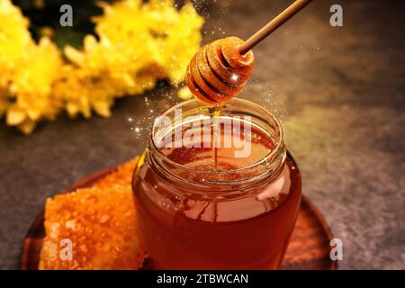 Natural honey dripping from dipper into glass jar on table under sunlight, closeup Stock Photo