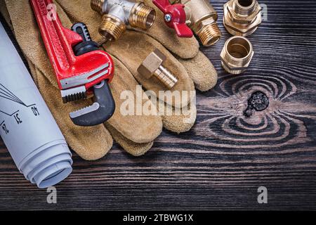 Leather protective gloves monkey wrench construction plans brass plumbing fittings gate valve on wooden board Stock Photo