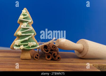 Christmas food and baking concept with a colorful glazed or iced cookies, cinnamon sticks and rolling pen over a festive blue background still life Stock Photo
