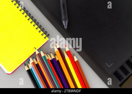 Digital stylus pen on digital graphic tablet for illustrators and designers opposite colored drawing pencils next to a wired notebook, Top view, free Stock Photo