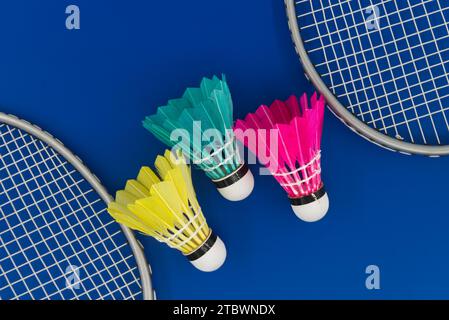 Badminton. Rackets and colorful feathered shuttlecocks in blue, yellow and pink on blue background in top view with free copy space Stock Photo
