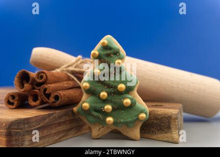 Christmas food and baking concept with a colorful glazed or iced cookies, cinnamon sticks and rolling pen over a festive blue background still life Stock Photo