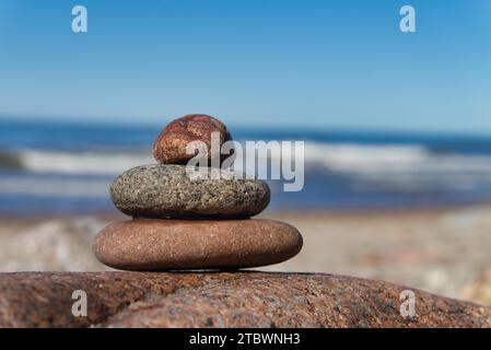 Stacked of stones or rocks on a beach placed on top of a boulder overlooking the ocean and gentle waves Stock Photo