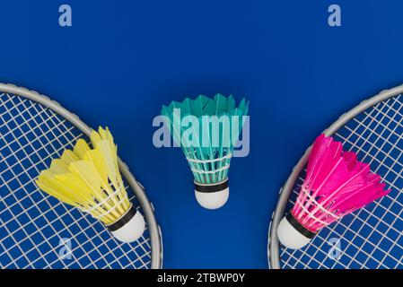 Badminton. Rackets and colorful feathered shuttlecocks in blue, yellow and pink on blue background in top view with free copy space Stock Photo
