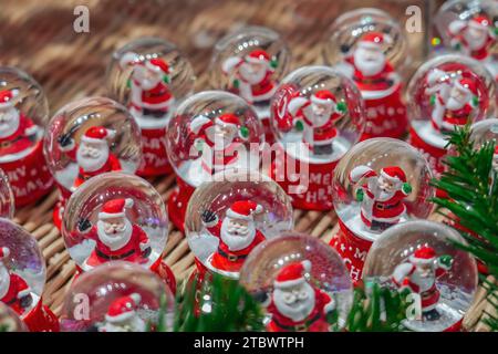 Lots of glass balls with Santa Claus and Christmas candy inside snow, fair, market. Stock Photo