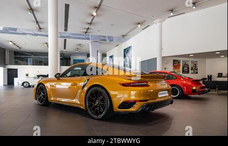 A picture of an orange Porsche 911 Turbo S next to a red Porsche 911 Carrera 3.0 inside a dealership Stock Photo