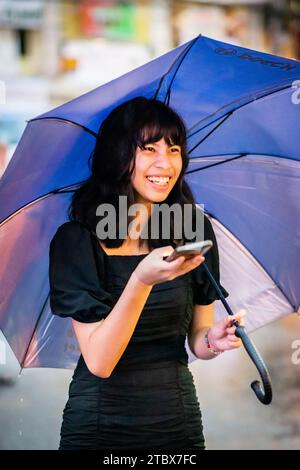 A beautiful Filipino girl keeps dry from the rain under an umbrella in Manila, The Philippines. Stock Photo